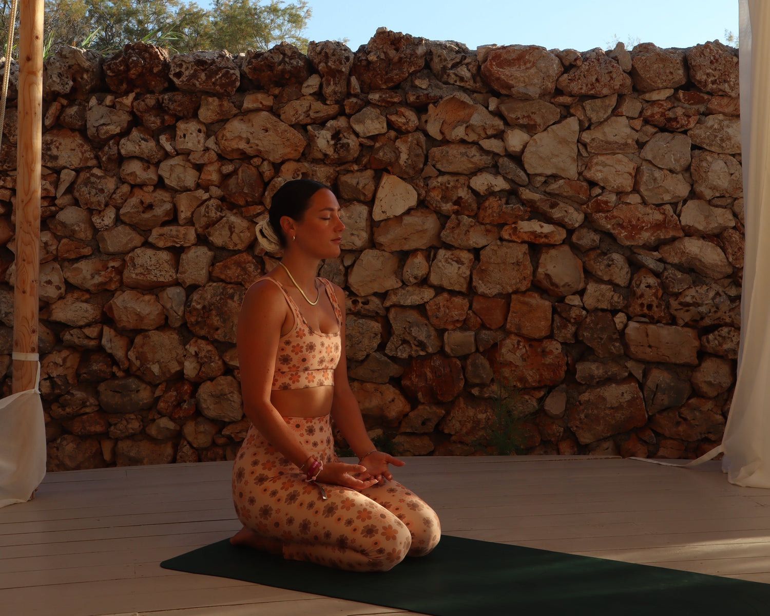 Person lying on a sunbed against a stone wall with a clear blue sky.